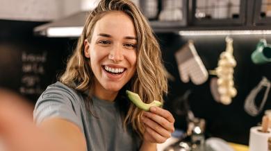 
		Frau lächelt in Kamera und isst Avocado
	